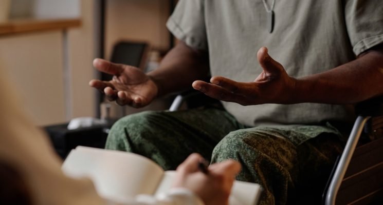 Black war veteran emotionally speaking during private therapy session, psychologist taking notes